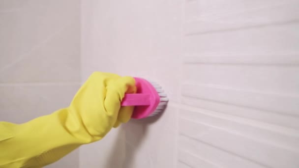 Tangan di sarung tangan karet membersihkan jahitan antara ubin di kamar mandi. — Stok Video