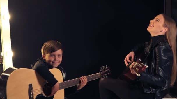 Ένα κορίτσι μαθαίνει σε ένα παιδί ένα αγόρι να παίζει κιθάρα. Ακουστική κιθάρα. Ευτυχισμένοι άνθρωποι. — Αρχείο Βίντεο