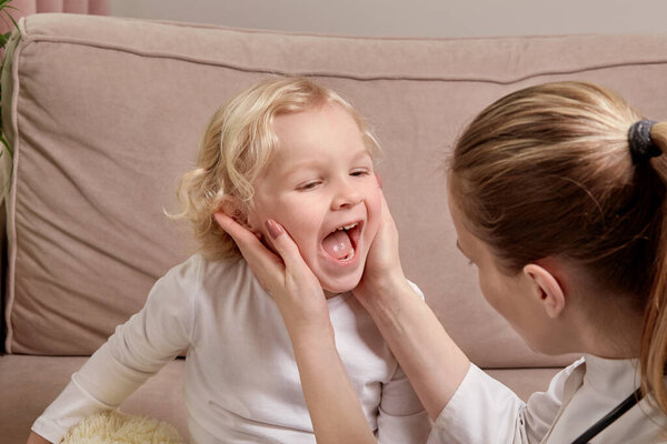 A woman doctor in a medical coat examines the throat of a child. Family doctor.