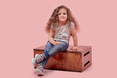 Küçük bir çocuk boş bir arka planda ahşap bir stantta oturur. Bebek sarışın..