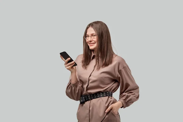 Una chica morena en ropa de moda se comunica usando un teléfono inteligente en línea . — Foto de Stock