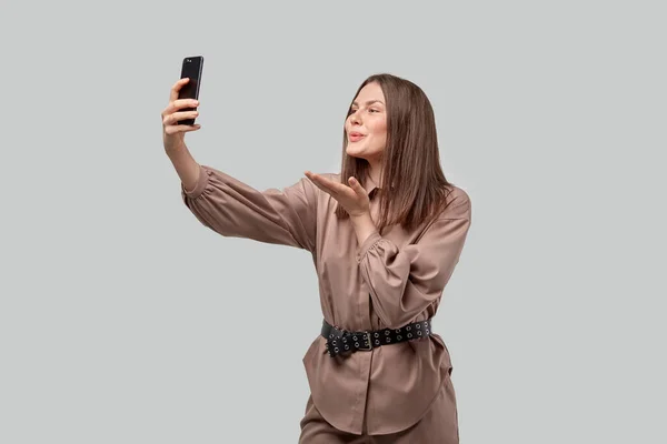 A brunette girl takes a selfie on her smartphone and sends an air kiss — Stock Photo, Image