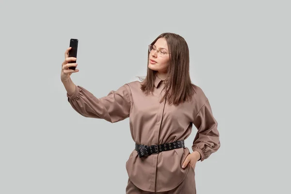 Hermosa chica morena en gafas para la vista hace selfie en un teléfono inteligente . — Foto de Stock