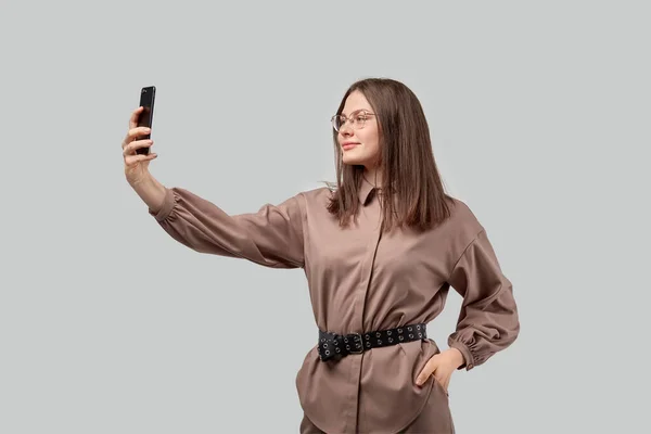 Una morena vestida con ropa de moda se toma una selfie en su smartphone . — Foto de Stock