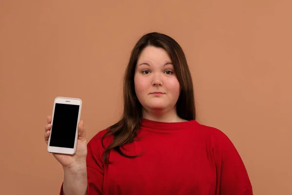 Una hermosa chica con sobrepeso muestra su teléfono móvil. Con una pantalla vacía . — Foto de Stock
