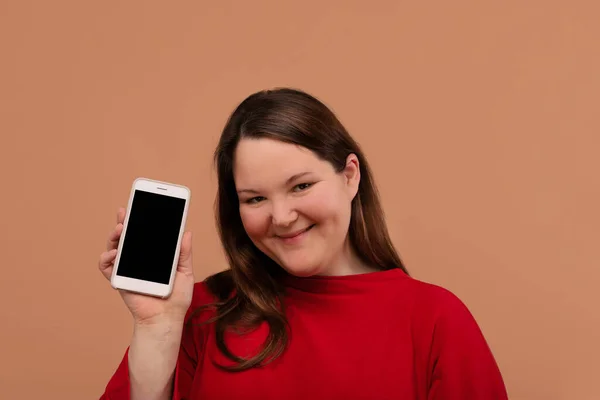 Una hermosa chica con sobrepeso muestra su teléfono móvil. Con una pantalla vacía . — Foto de Stock