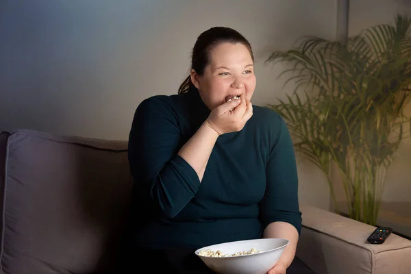 Usmívající se dívka s nadváhou v obýváku se dívá na televizi s popcornem. — Stock fotografie