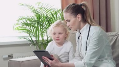 Doktor çocuğa çocuğun tablette oynadığını gösteriyor. Aile doktoru.