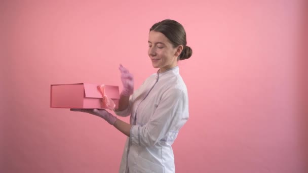 Beautiful brunette girl in a medical coat with an open gift box in her hands. — Stock Video