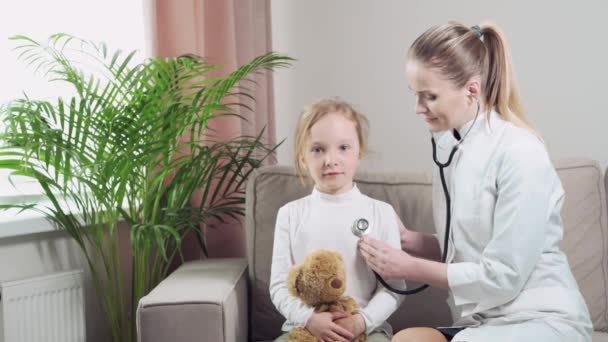 Девушка, сидящая на диване. Доктор слушает фонендоскоп для дыхания — стоковое видео