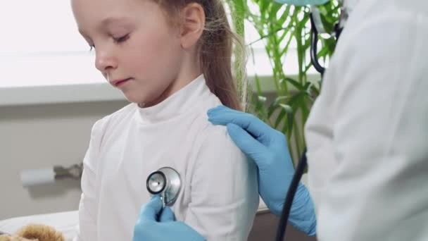 Dokter mendengarkan napas fonendoskop seorang gadis pirang. Gadis itu demam. — Stok Video