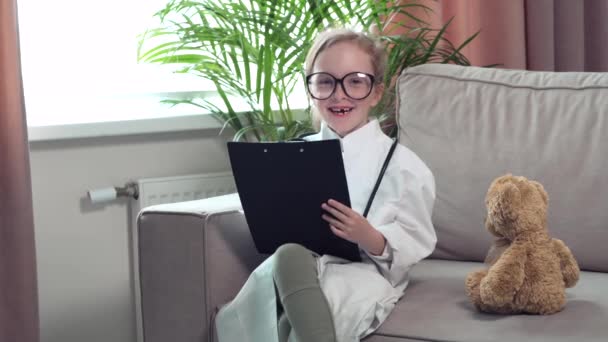 Une fille en manteau médical. Un enfant avec des lunettes joue un médecin. — Video
