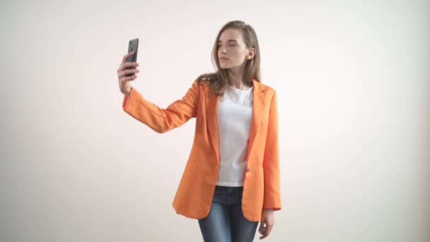 Jeune fille brillante regardant la caméra et prenant un selfie. Fond blanc. — Video
