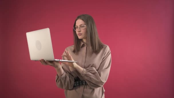 En vacker flicka med ett överraskat ansikte tittar in i en bärbar dator. Röd bakgrund. — Stockvideo