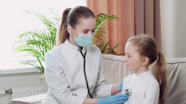 Médico con guantes médicos y máscara escucha la respiración del niño con un fonendoscopio . — Vídeos de Stock