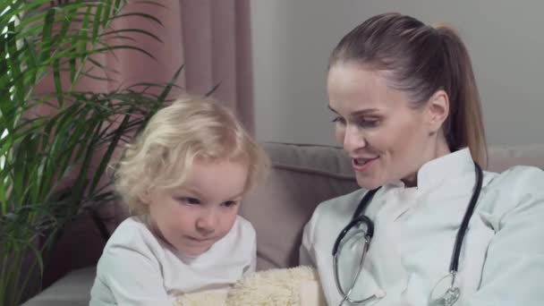 Doctor kinderarts praten terwijl zitten op een bank met een schattig blond kind. — Stockvideo