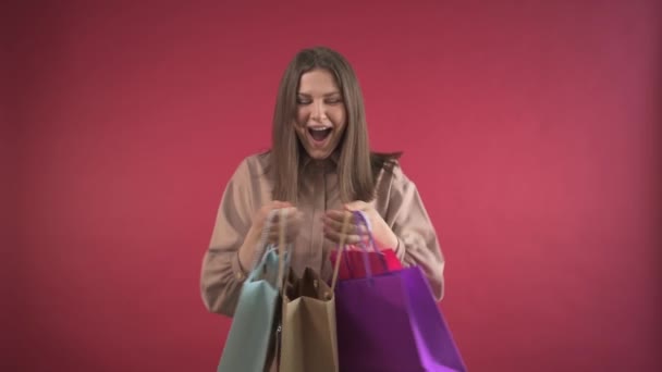 The girl opens the gifts that she gave and is very happy. red background. — Stock Video