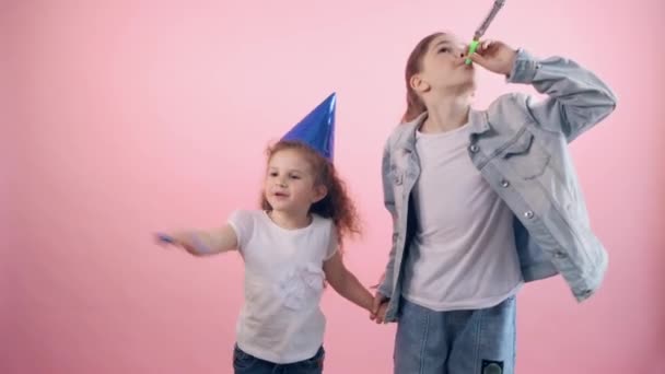 Dos hermanas ríen y suenan en un silbato festivo. Celebrar un cumpleaños juntos . — Vídeo de stock