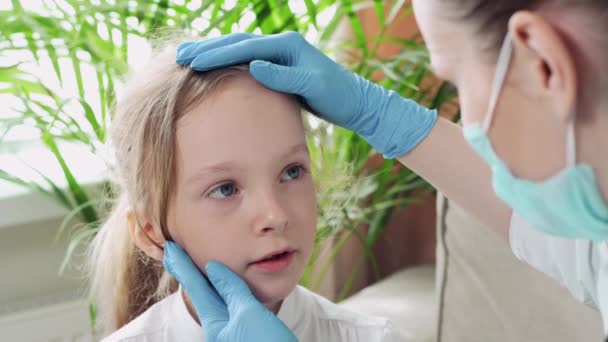 Mujer hermosa joven médico examina a un niño enfermo en casa, sentado en un sofá . — Vídeos de Stock