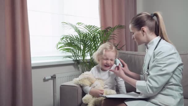 El médico comprueba la audición del niño con un otoscopio. Lindo bebé rubia esquiva — Vídeos de Stock