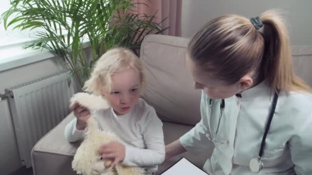 Sevimli sarışın bir bebek en sevdiği oyuncağıyla oynar ve bir çocuk doktoruyla konuşur.. — Stok video