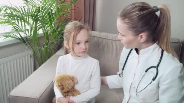 Jeune belle femme médecin examine un enfant malade à la maison, assis sur un canapé. — Video