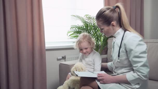 Badanie dziecka w domu, siedzącego na kanapie przez lekarza w szlafroku medycznym. — Wideo stockowe