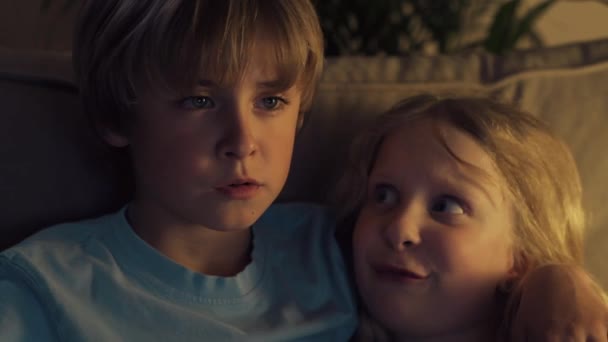 El chico abrazó a la chica y está viendo la televisión. Niños rubios están discutiendo dibujos animados . — Vídeos de Stock