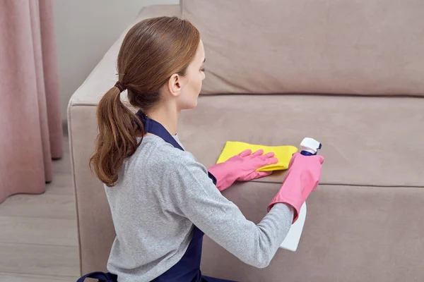 Menina senta-se e aplica um limpador de spray para móveis. Limpeza da sala de estar . — Fotografia de Stock