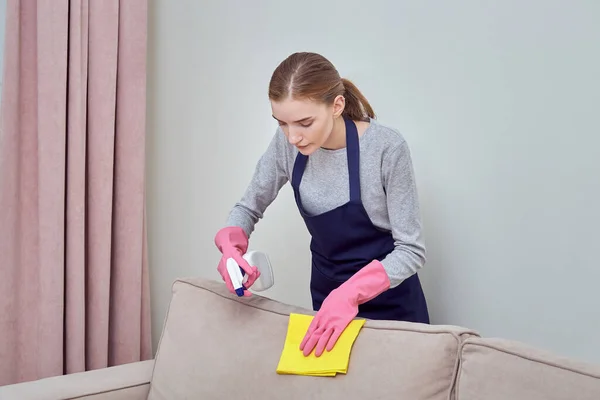 Limpeza de casa profissional. Uma menina de luvas aplica agente de limpeza para o sofá — Fotografia de Stock