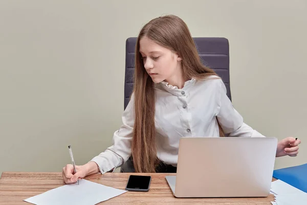 Una hermosa chica se sienta en una oficina con una computadora portátil y escribe información en papel — Foto de Stock