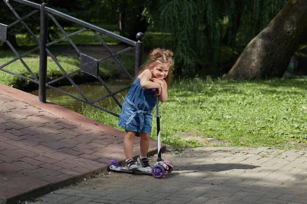 Boldog gyönyörű, aranyos kislány, aki robogózik a parkban.. — Stock Fotó