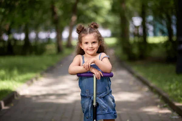 Menina bonita monta uma scooter no parque. Menina morena bonita . — Fotografia de Stock