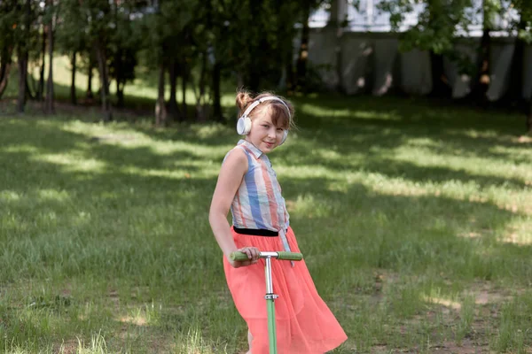 Retrato de uma linda garota bonita que está montando uma scooter no parque . — Fotografia de Stock