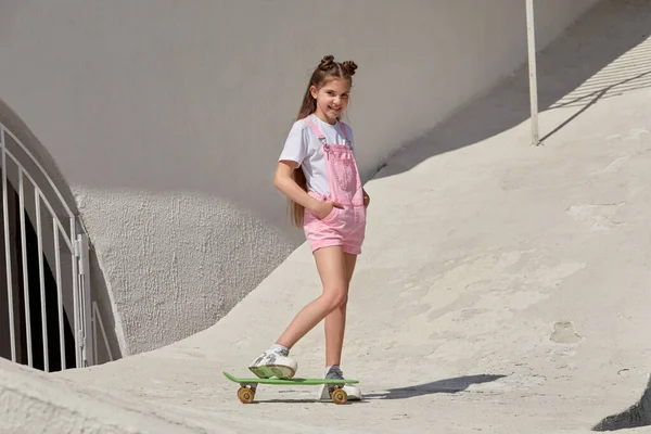 Красивая стройная девушка со скейтбордом на фоне светлого здания. — стоковое фото