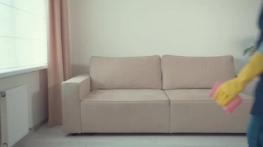 Önlüklü ve eldivenli bir kız kanepeye oturur, ürünü temizlemek için sprey kullanır..