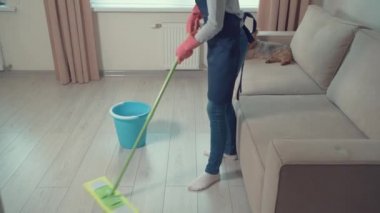 Oturma odasında lastik eldivenlerle yerleri paspaslıyor..