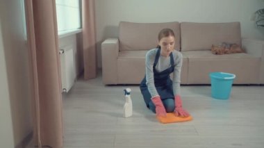 Dizlerinin üstünde oturan bir kız evdeki kimyasallarla yerleri yıkıyor..