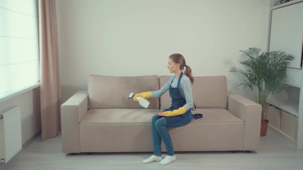 Chica se sienta en un sofá en una hermosa habitación acogedora y lava muebles tapizados . — Vídeos de Stock