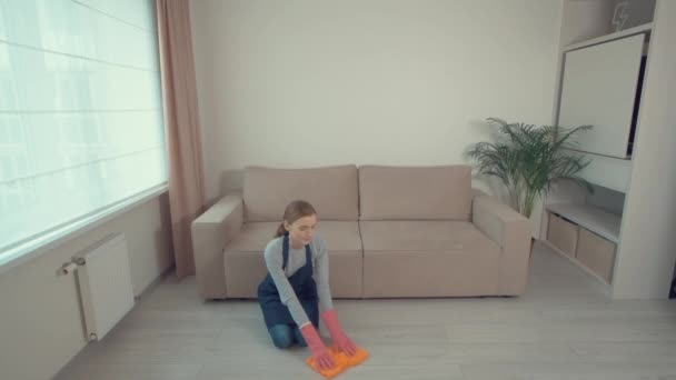 Молода красива дівчина, що сидить на підлозі, миє підлогу ганчіркою . — стокове відео
