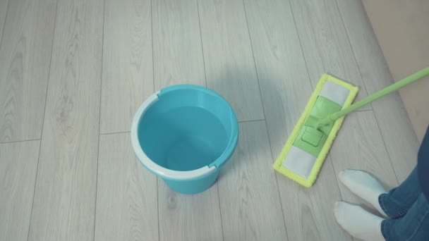 Girl washes the floor in the living room with a mop, next to a bucket of water. — Stock Video