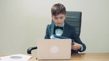 Yakışıklı adam içinde belgeler olan bir klasörü açıyor. Masada bir dizüstü bilgisayar var..