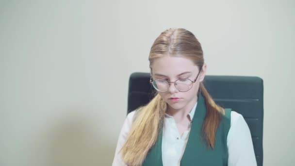 Portret młodej dziewczyny w okularach, siedzącej w biurze, w miejscu pracy — Wideo stockowe