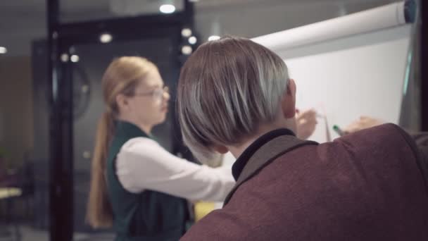 La vue arrière de la personne qui dessine un graphique sur le tableau.