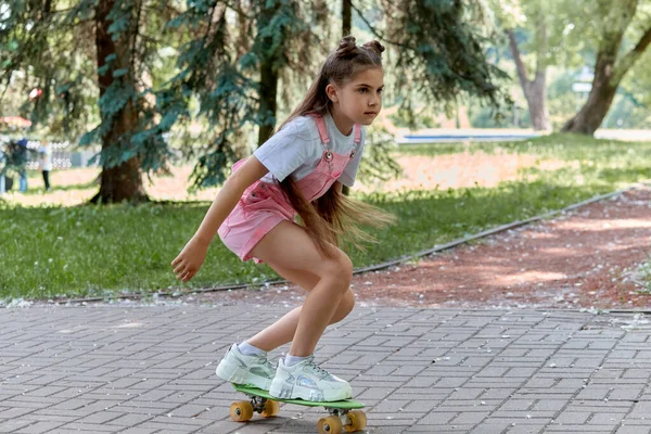 Hezká brunetka jezdí na prkně v parku. Sportovní životní styl. Letní prázdniny. — Stock fotografie