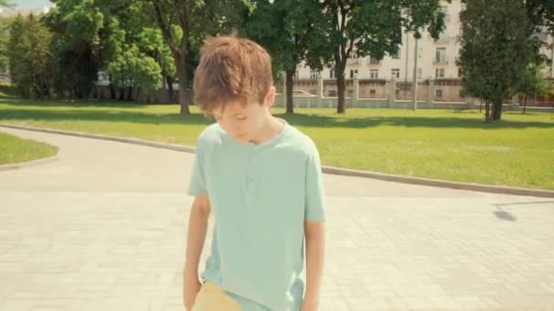 도시에서 스케이트보드를 타고 있는 갈색 머리 소년이 있습니다. 태양이 내리는 날씨. — 비디오
