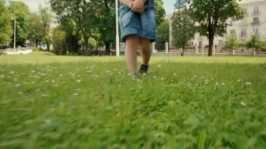 Kırık dizli bir çocuk yaz çimlerinde yürüyor. Parlak yeşil çimenler.