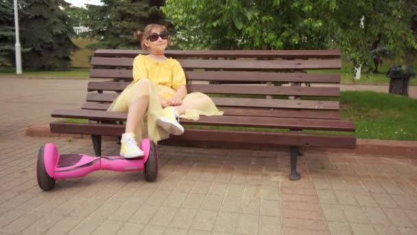 Gyönyörű lány ruhában és napszemüvegben, lábak egy giroszkóp alatt. Nyári park. — Stock videók