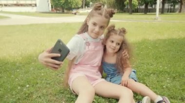 İki güzel kız, uzun saçlı, yeşil çimlere oturup selfie çekiyorlar..