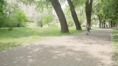 Esmer bir kız yaz parkında scooter kullanıyor. Kavak tüyü ve toz uçuyor